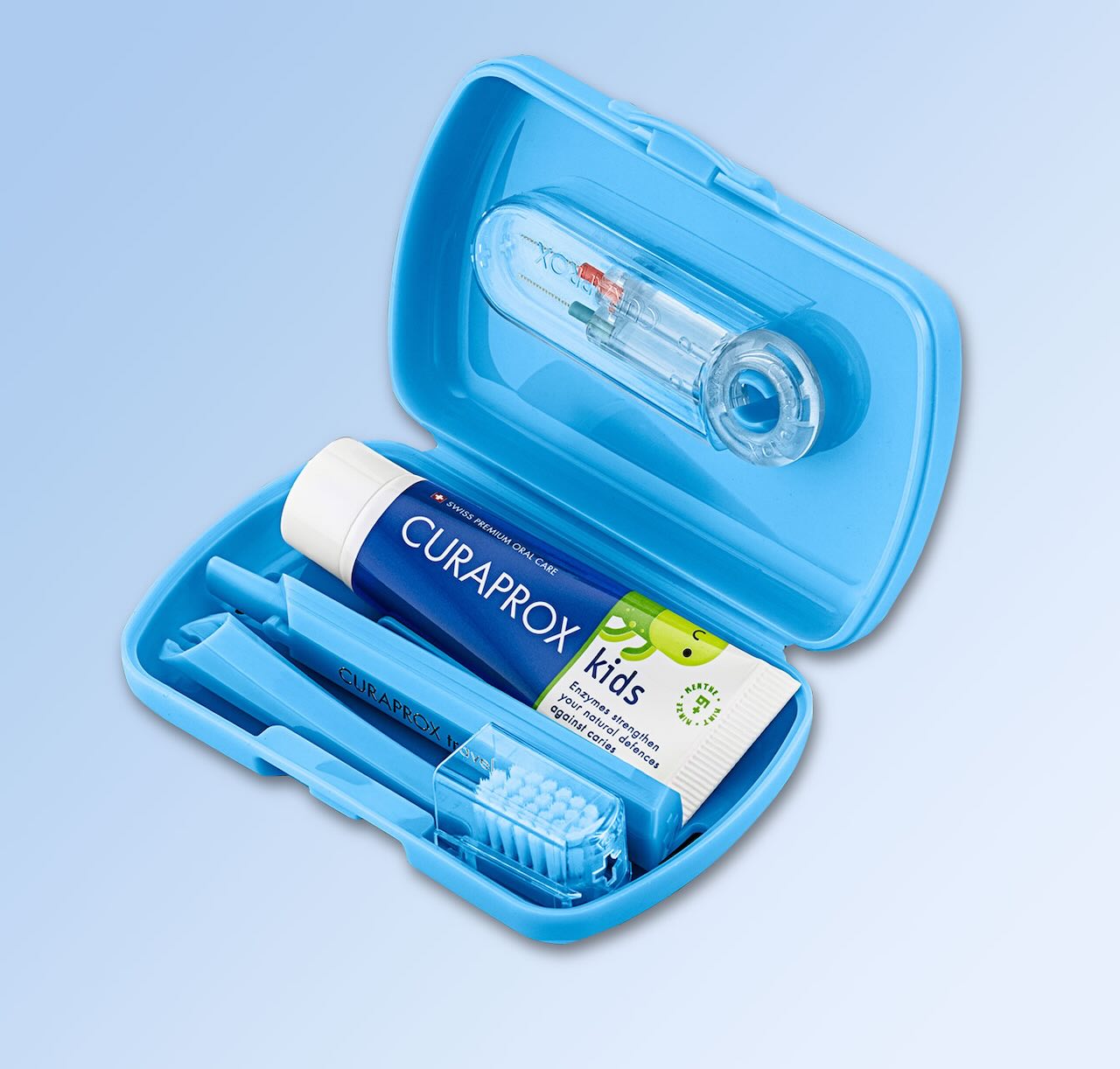 Das offene blaue Kids Travel Set zeigt im Deckel zwei Interdentalbürsten, im Boden liegen eine Kids-Zahnpasta und die geteilte Kids-Handzahnbürste. Alle Produkte sind von Curaprox.