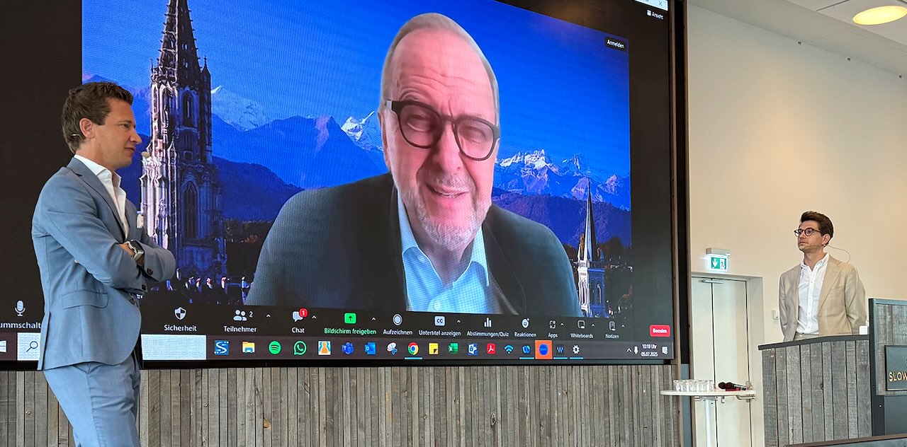 Zwei Referenten Prof. Dr. Dr. Eik Schiegnitz und Dr. Frederik Hofmann stehen vor einer großen Videowand, auf der Prof. Dr. Daniel Buser zu sehen ist.