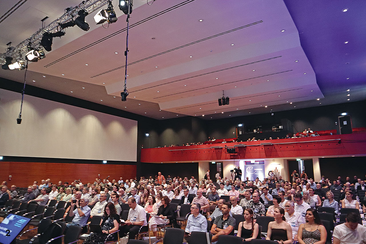 Viele Menschen sitzen in einem Vortragssaal, Blick von der Bühne auf das Publikum