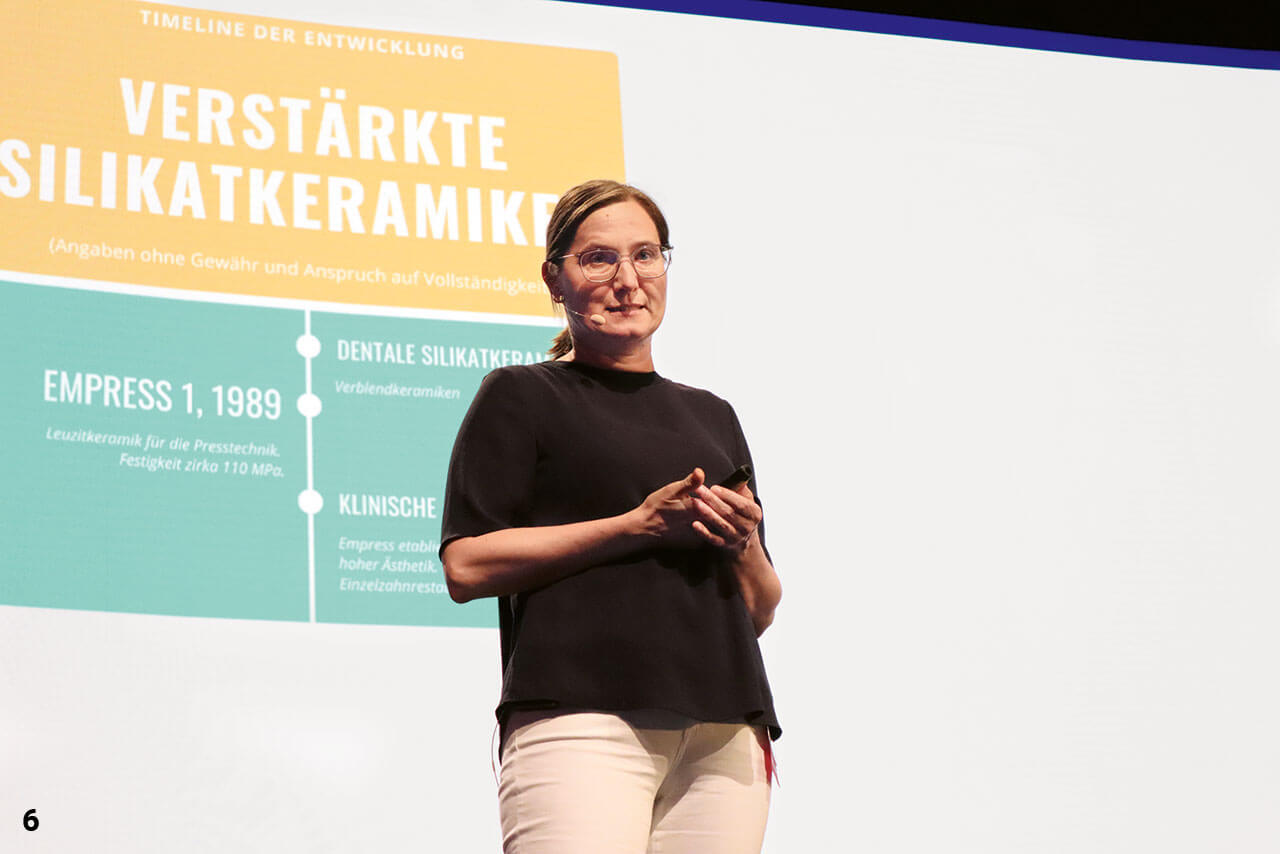 Prof. Dr. Bogna Stawarczyk auf der Bühne der Stadthalle Nürtingen vor einer Leinwand mit einer farbigen Grafik (oben gelb, unten türkis).