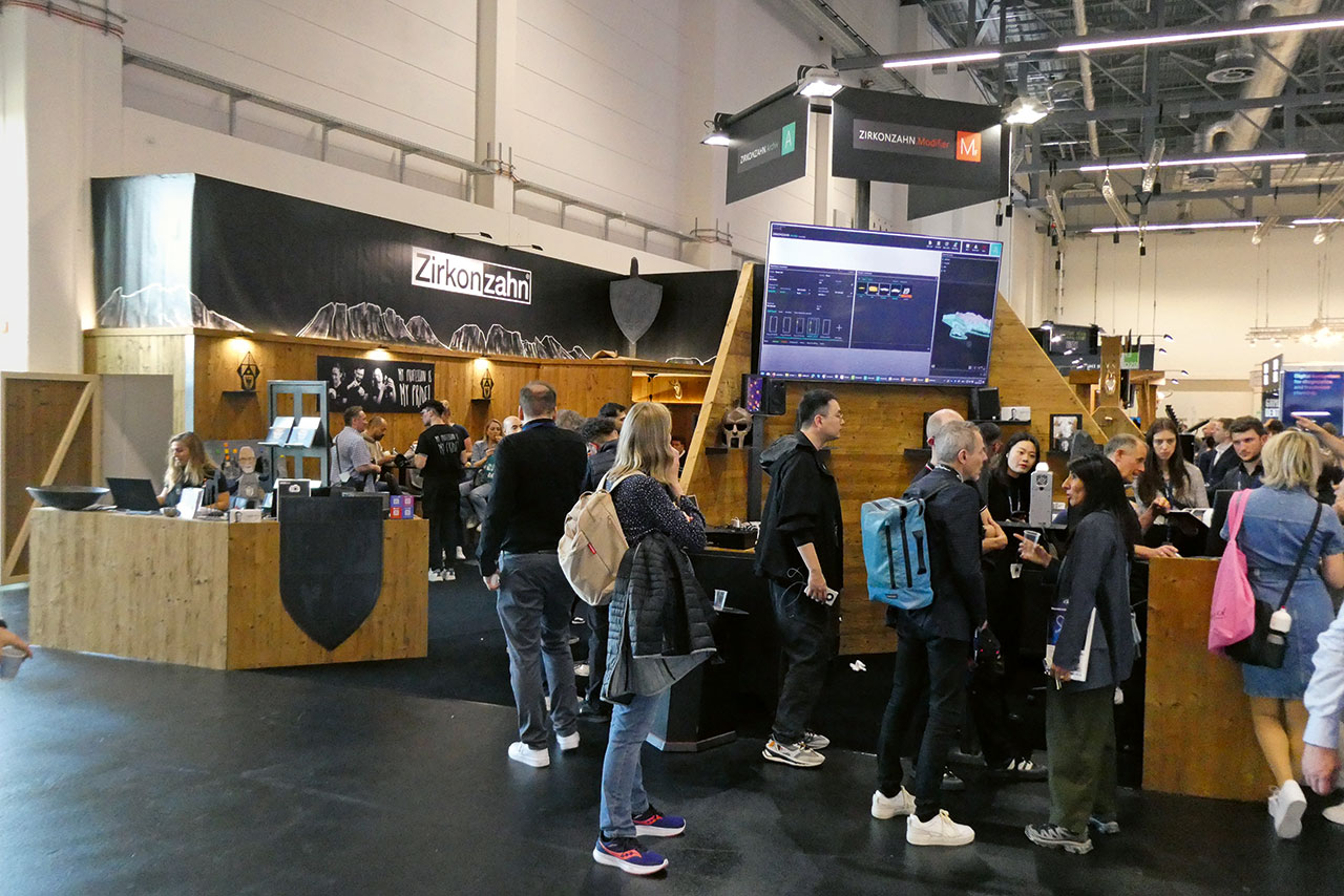 Messebesuchende vor dem mit Holz verkleideten Stand von Zirkonzahn, rechts im Hintergrund ein großer Bildschirm, dass den Screenshot einer Dentalsoftware zeigt.