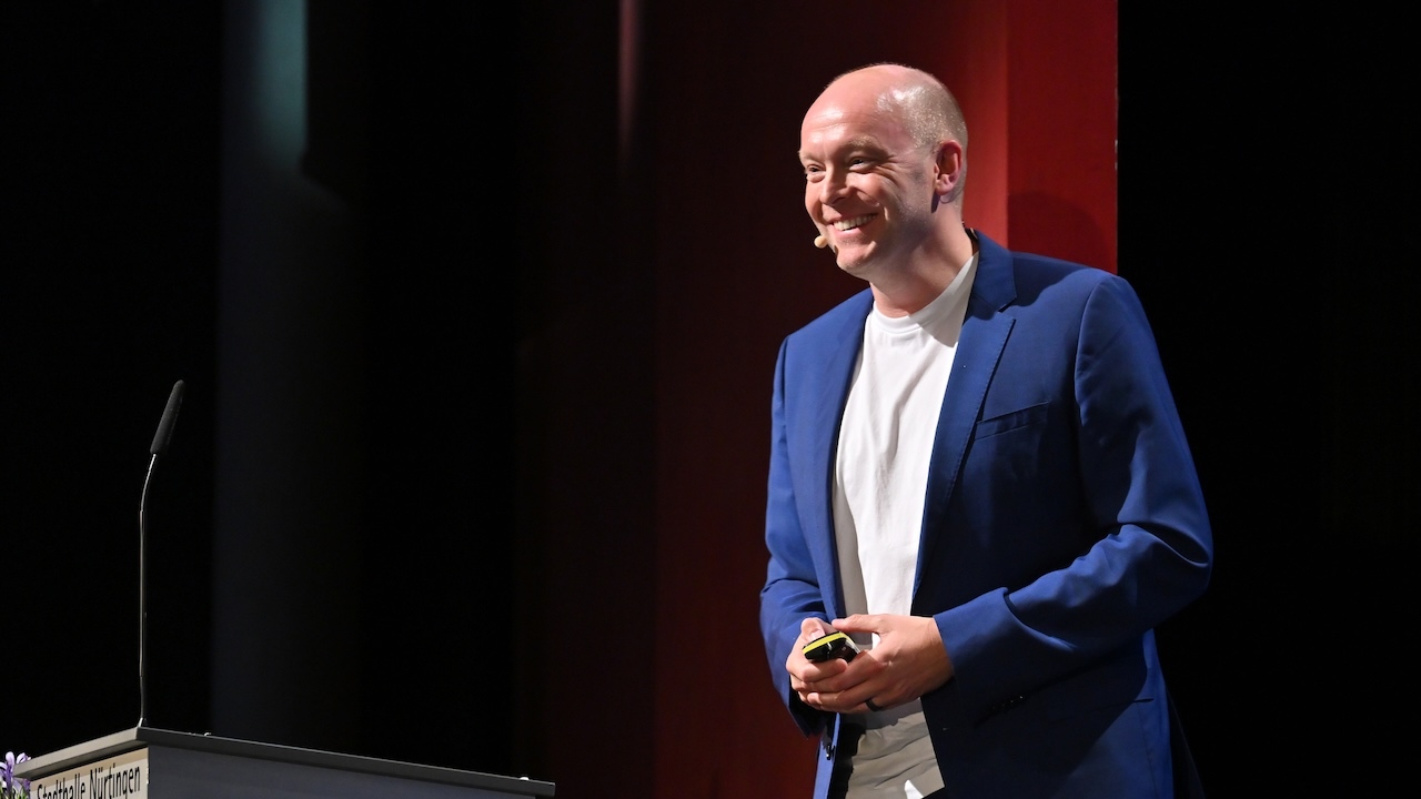 Prof. Florian Beuer auf der Bühne der Stadthalle Nürtingen vor rotem Vorhang.