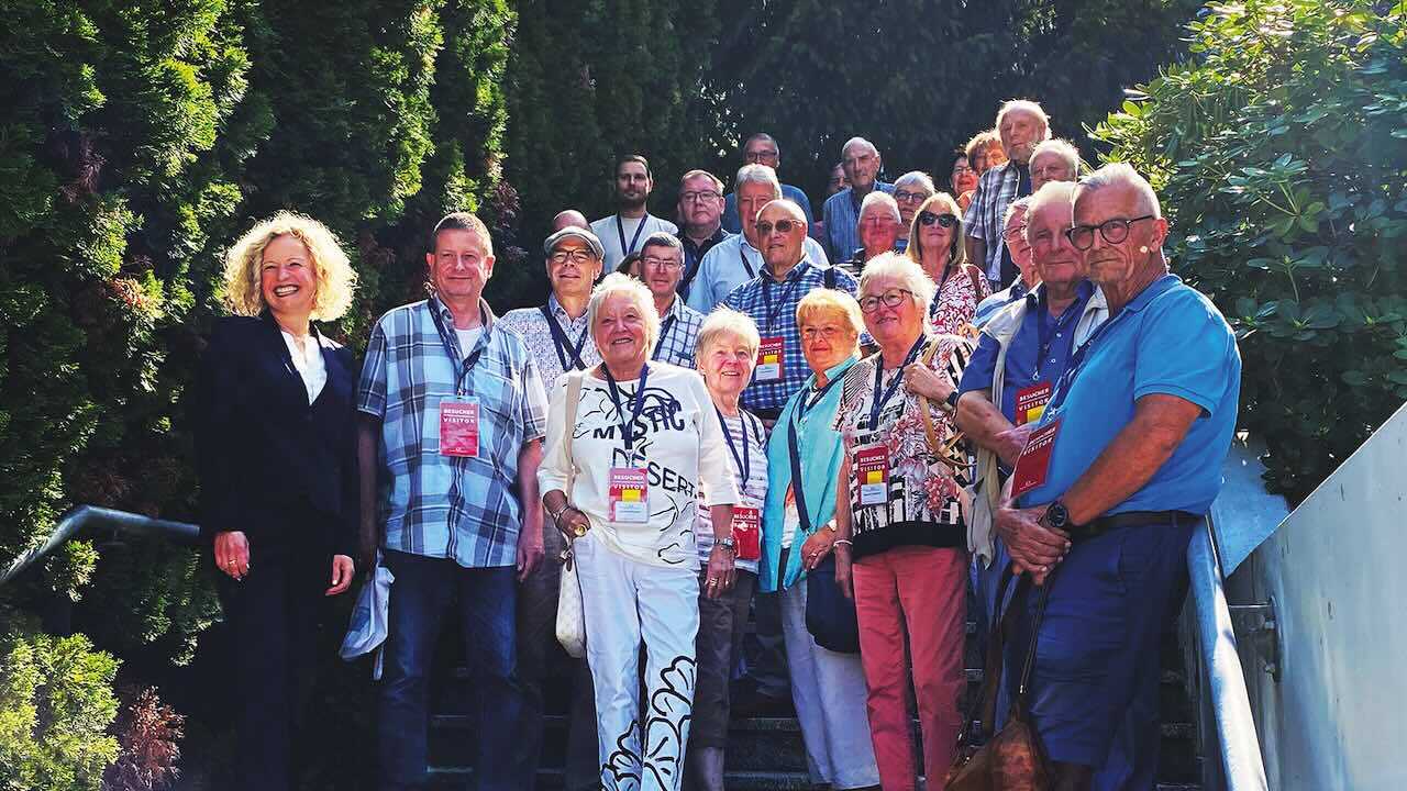 Die Besucher in sommerlicher Kleidung stehen mit Geschäftsführerin Claudia Stöhrle zusammen auf einer Treppe. Im Hintergrund sind Sträucher und Nadelbäume zu sehen.